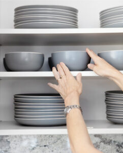 Hands placing dishes on an overhead shelf