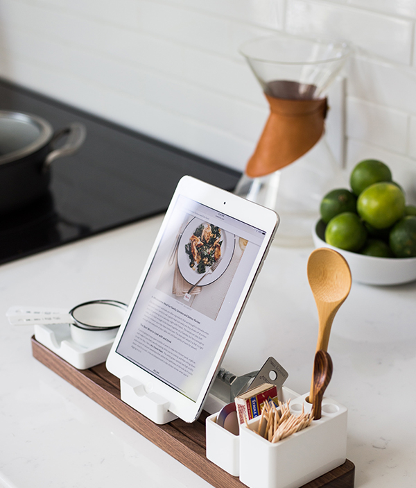 iPad in a holder with bowl of limes and decorative items on kitchen counter